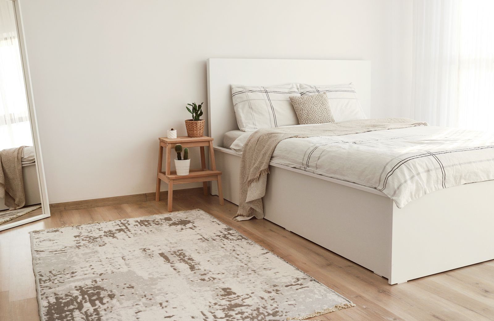 Light-filled bedroom with neutral linen, natural wood and a quiet seating corner